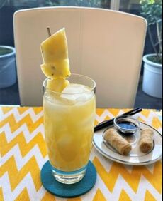 Cocktail with Pineapple and a plate of egg rolls on a table