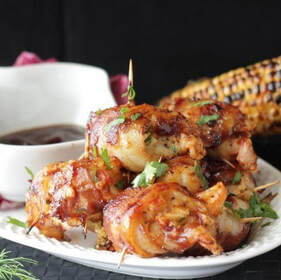 Bacon wrapped crab stuffed shrimp on a plate with dipping sauce and grilled corn on the cob