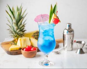 Blue Hawaii Cocktail with pineapple, cherries, shaker and jigger in the backgroundcture