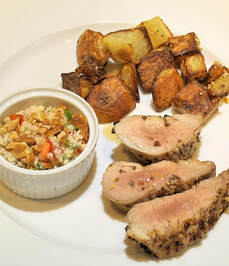 Plate with 3 pieces of roast pork tenderloin, a pile of roasted potatoes and a cup of cous cous