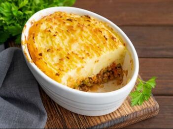 Dish of Shepherd's Pie with scoop taken out, sitting on a board with towel and parsley in background