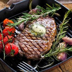 Steak with butter, rosemary and tomatoes in pan